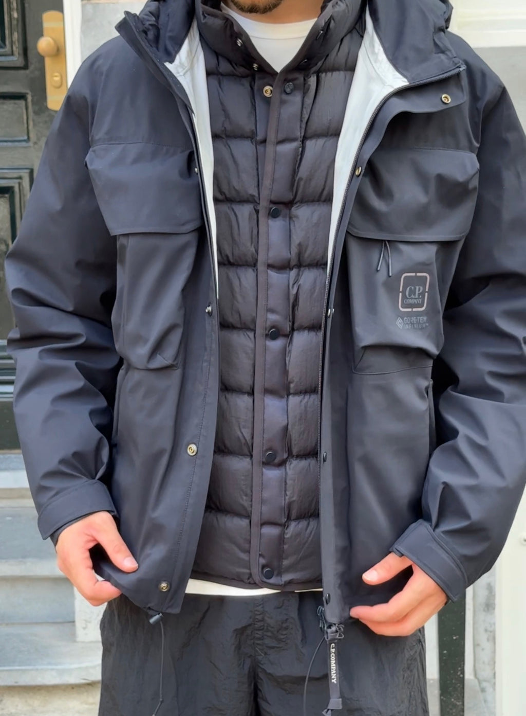 Model with black wind jacket open and black down jacket visible