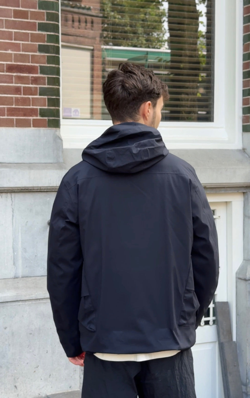 Back side of model with black hooded wind jacket