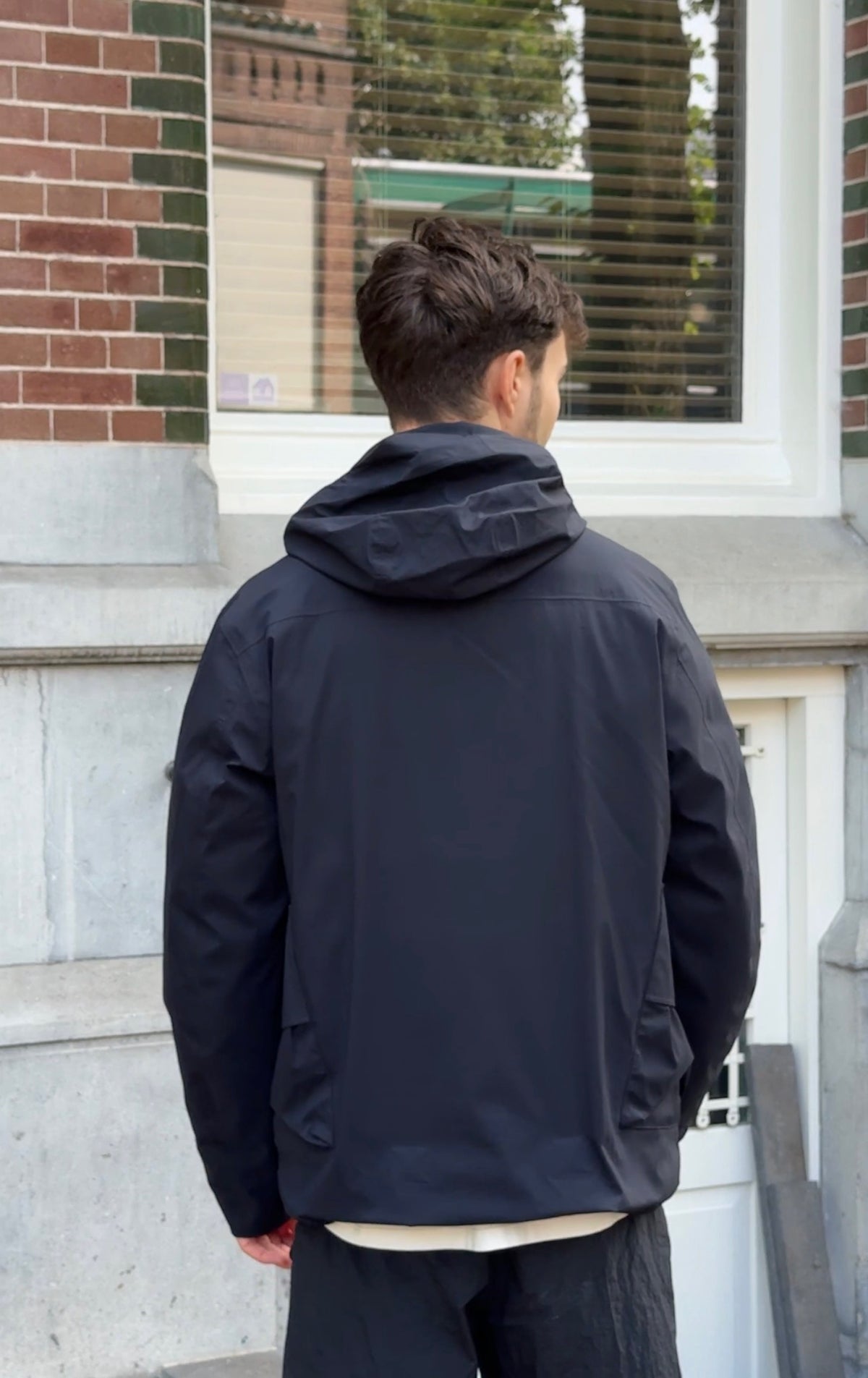 Back side of model with black hooded wind jacket