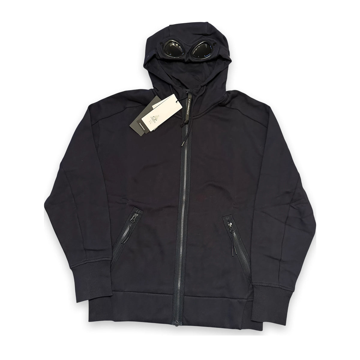 A black hooded zip-up jacket with integrated goggles on the hood, shown flat against a white background with a paper tag attached.