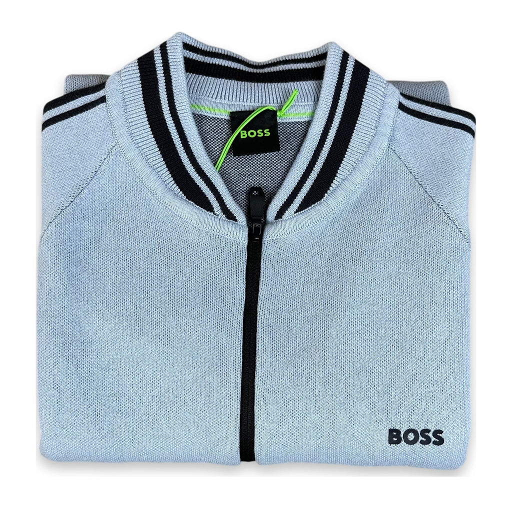 A folded light blue knit zip-up sweater with black and white striped ribbed collar and cuffs, featuring a black zipper and a black BOSS logo on the lower right front.