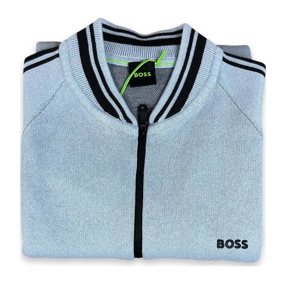 A folded light blue knit zip-up sweater with black and white striped ribbed collar and cuffs, featuring a black zipper and a black BOSS logo on the lower right front.