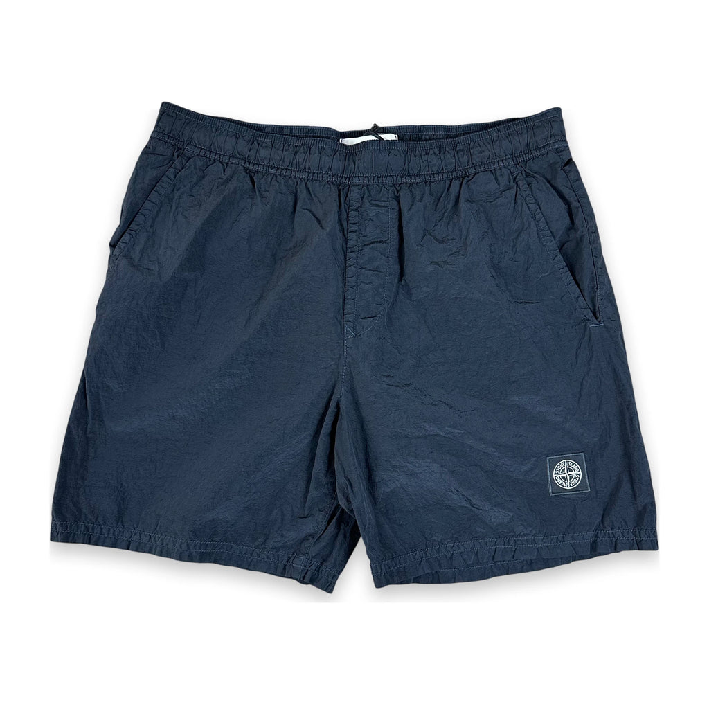 A pair of dark navy blue shorts with an elastic waistband, side pockets, and a small Stone Island logo patch on the lower left leg, shown against a plain white background.