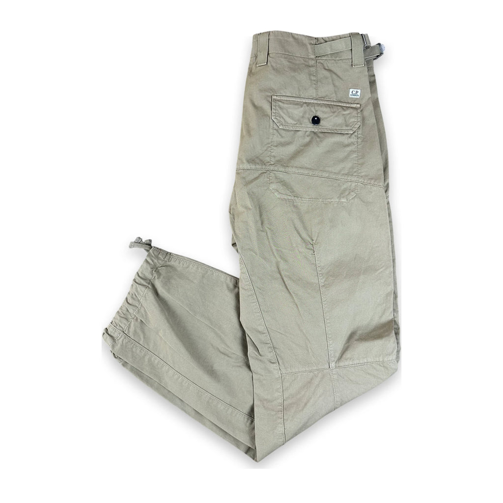 A pair of light khaki cargo pants laid flat on a white background, featuring a buttoned cargo pocket and elasticized ankle cuffs.