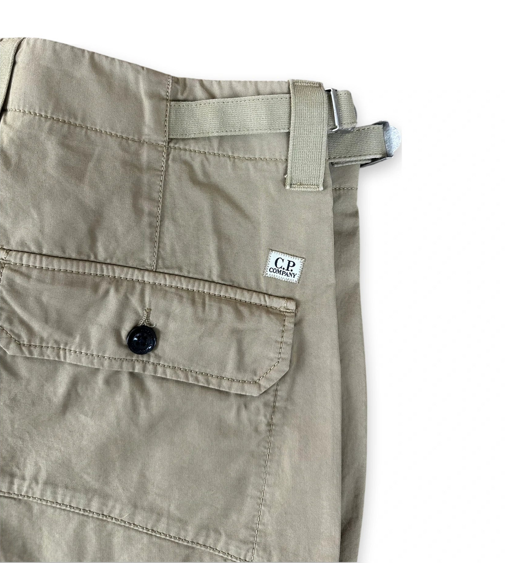 Close-up of folded khaki cargo pants showing a side pocket with a button, belt loop, and a small white C.P. Company label.