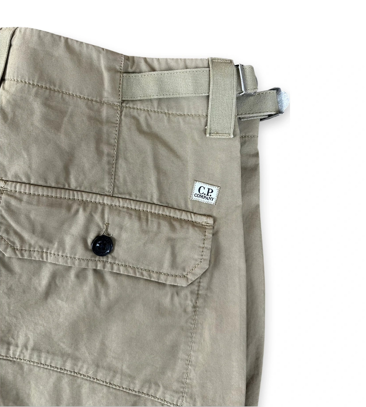 Close-up of folded khaki cargo pants showing a side pocket with a button, belt loop, and a small white C.P. Company label.