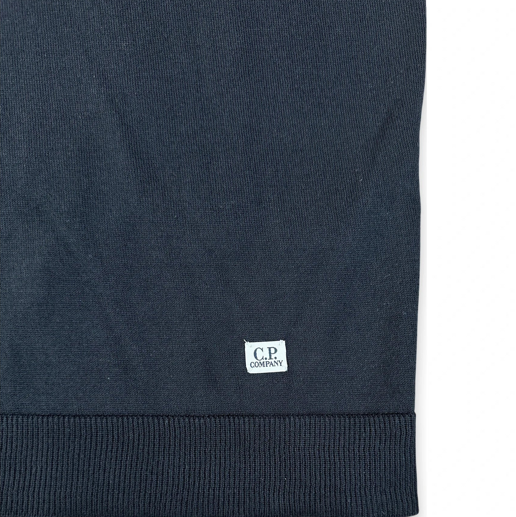 Close-up of a dark navy ribbed knit garment, likely a sweater or sweatshirt, showing a small white C.P.