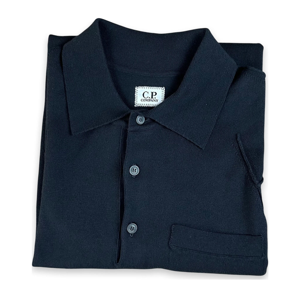 A folded dark navy blue polo shirt with a collar, three-button placket, and a chest pocket, displayed on a clean white background. The neck label shows the brand 'C.P. Company'