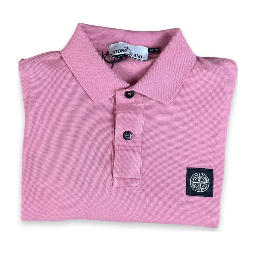 A folded pink Stone Island polo shirt with a black button placket and a black woven compass logo patch on the left chest, shown on a white background.