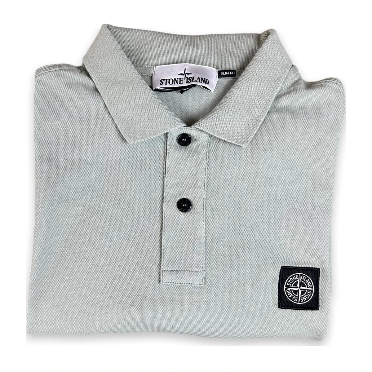 A folded Stone Island polo shirt in light gray, featuring a classic collar, two black buttons, and the signature compass logo patch on the left chest.