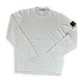 A long-sleeve crewneck shirt in off-white cotton, featuring the black and yellow Stone Island compass patch on the left sleeve, laid flat on a white background.