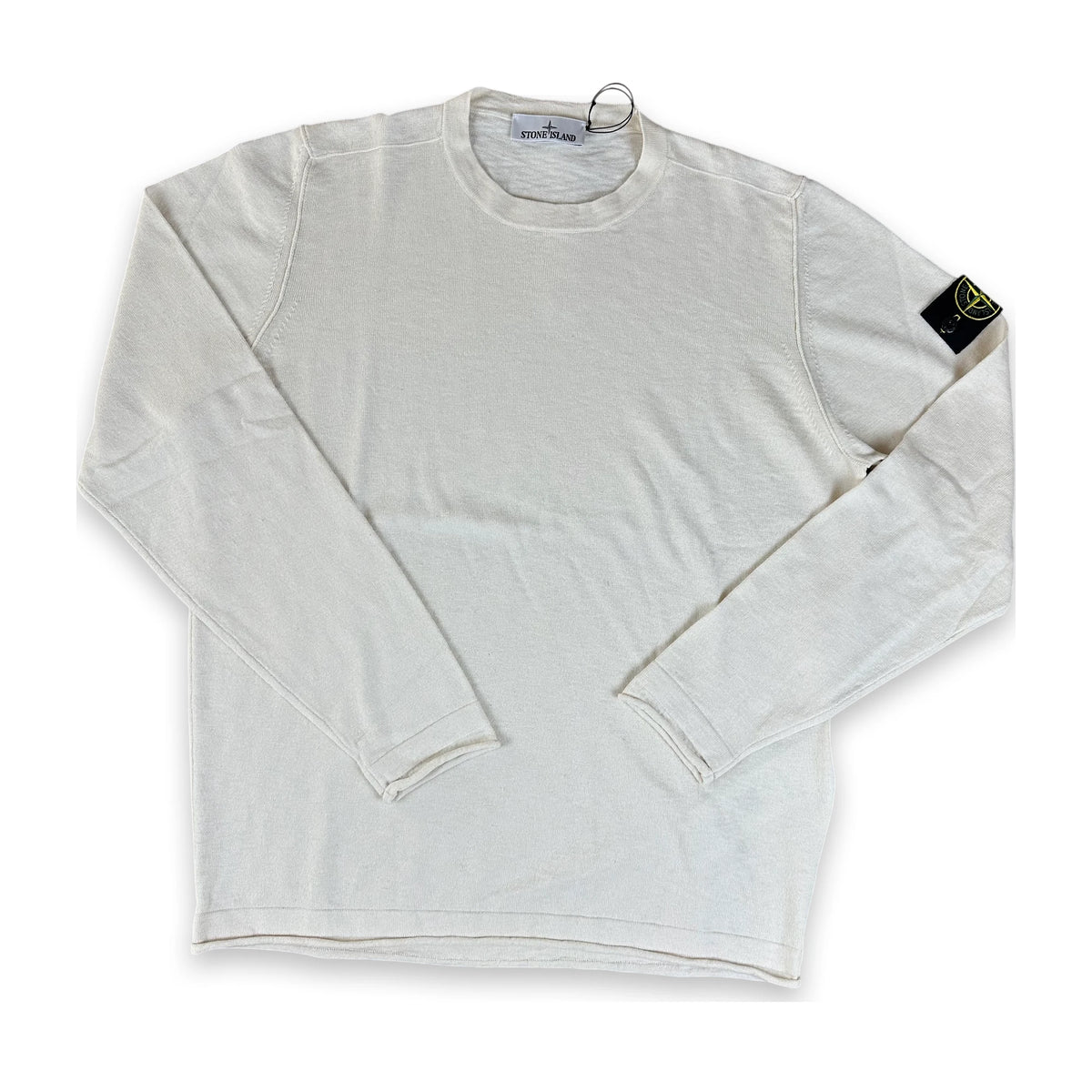 A long-sleeve crewneck shirt in off-white cotton, featuring the black and yellow Stone Island compass patch on the left sleeve, laid flat on a white background.