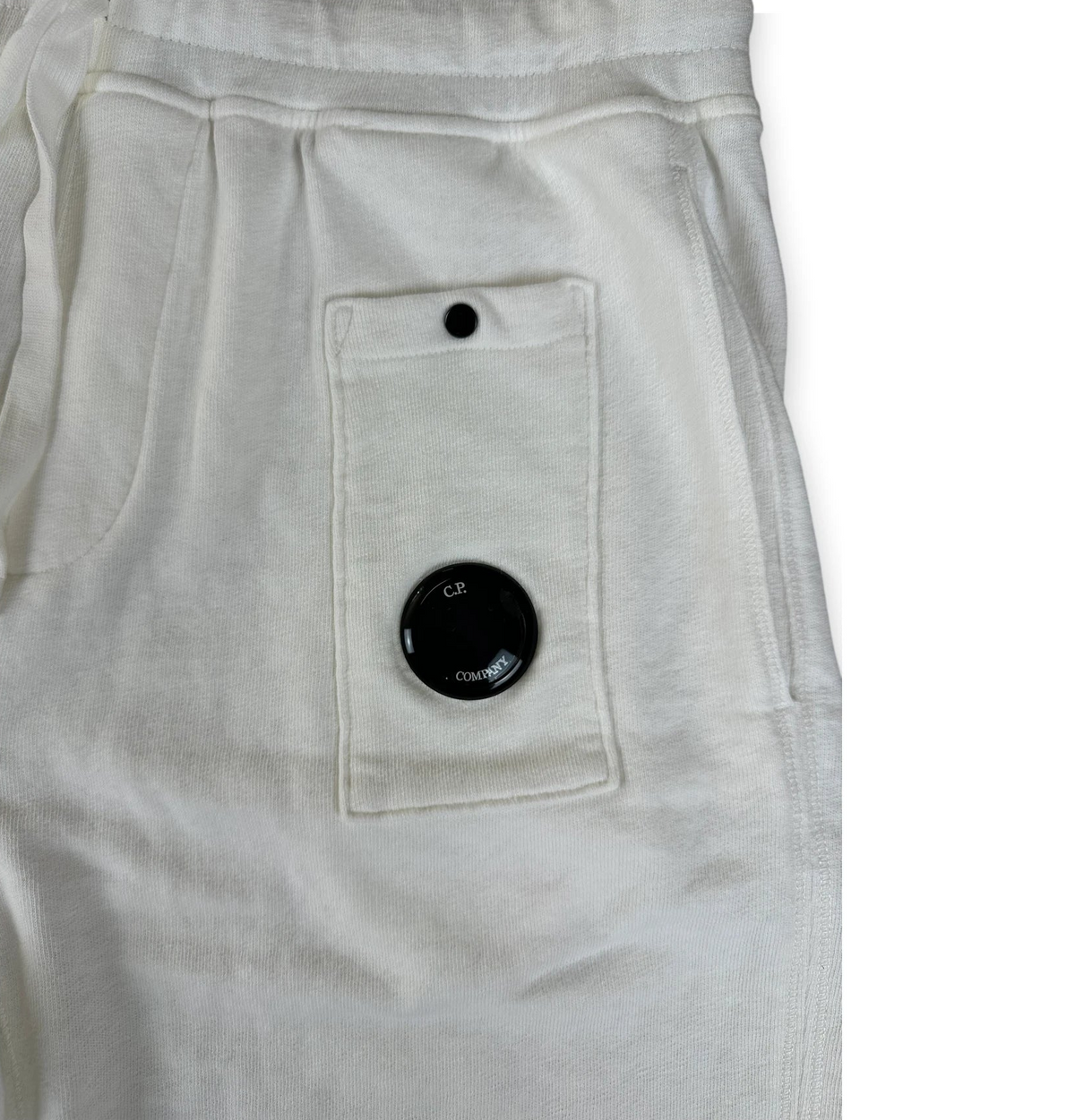 Close-up of off-white sweatpants showing a back pocket with a black snap button and a circular black dial detail.