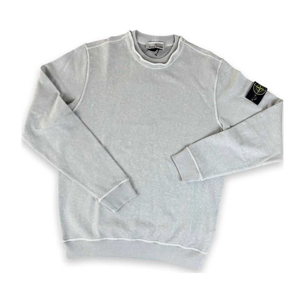 A light gray heather crewneck sweatshirt with white contrast stitching, featuring the Stone Island compass patch on the left sleeve, laid flat on a white background.