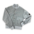 A light gray nylon utility jacket with a stand-up collar, button closure, and front flap pockets, laid flat on a white background.