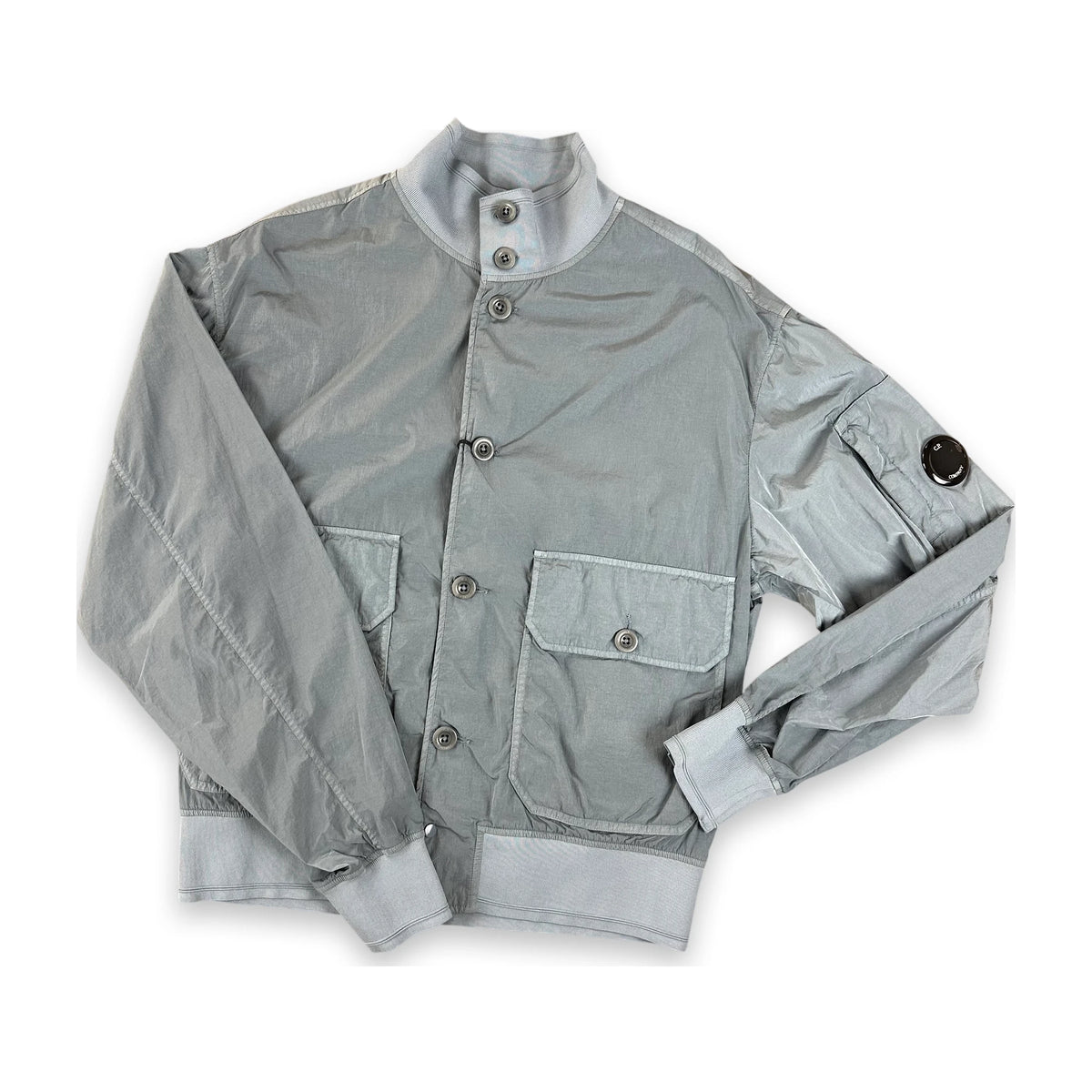 A light gray nylon utility jacket with a stand-up collar, button closure, and front flap pockets, laid flat on a white background.