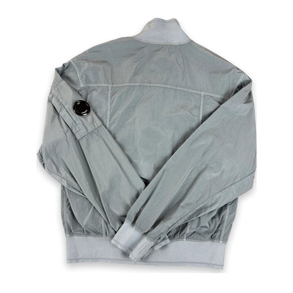 A light gray lightweight jacket shown from the back, featuring a high collar, a black snap button detail on the upper sleeve, and elasticized cuffs and hem, laid flat on a white background.
