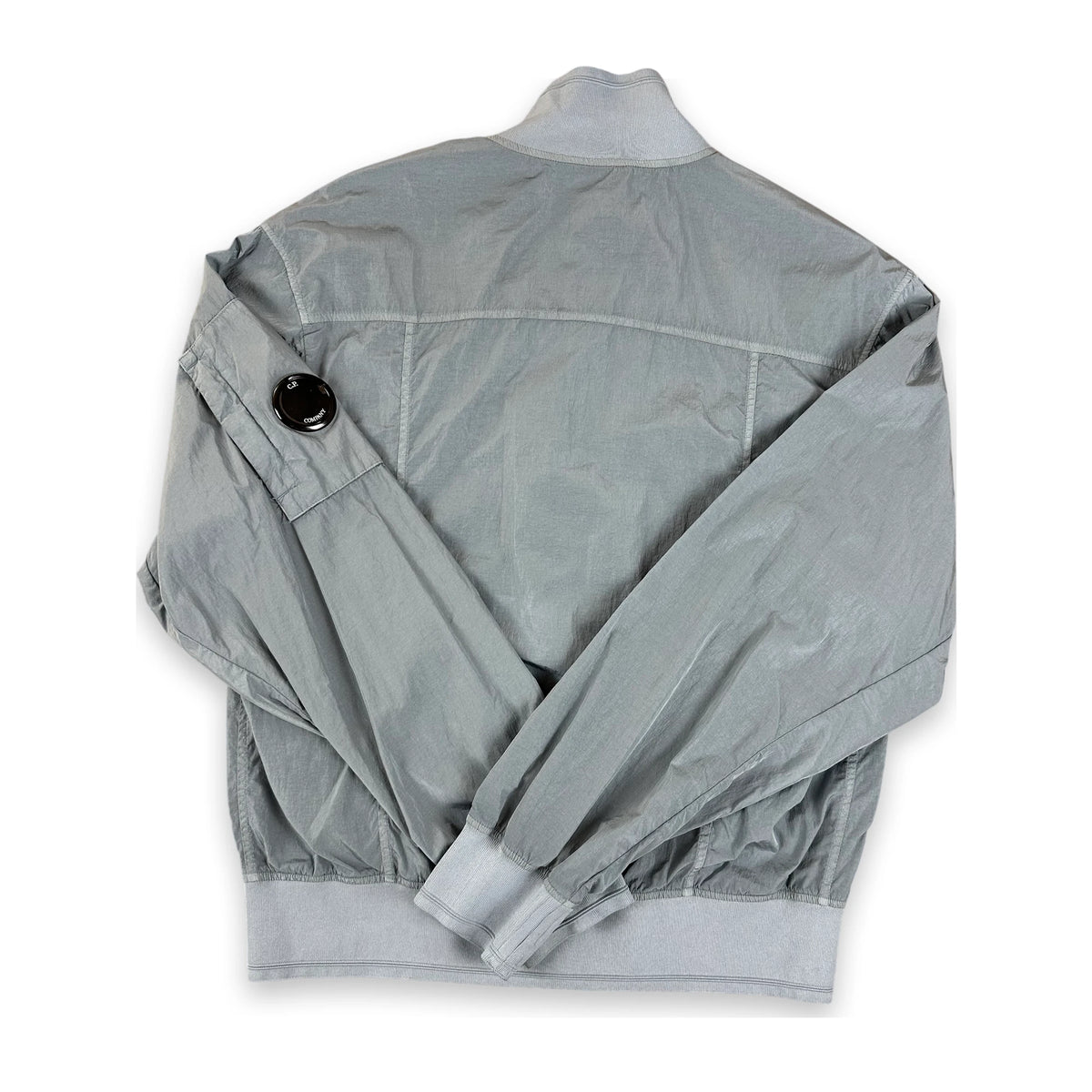 A light gray lightweight jacket shown from the back, featuring a high collar, a black snap button detail on the upper sleeve, and elasticized cuffs and hem, laid flat on a white background.