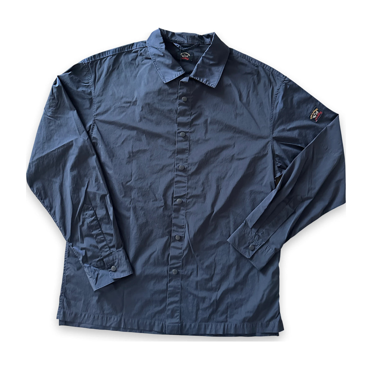 A dark navy blue long-sleeve button-up shirt laid flat on a white background, featuring a classic collar, button front, and a small embroidered logo on the left sleeve.