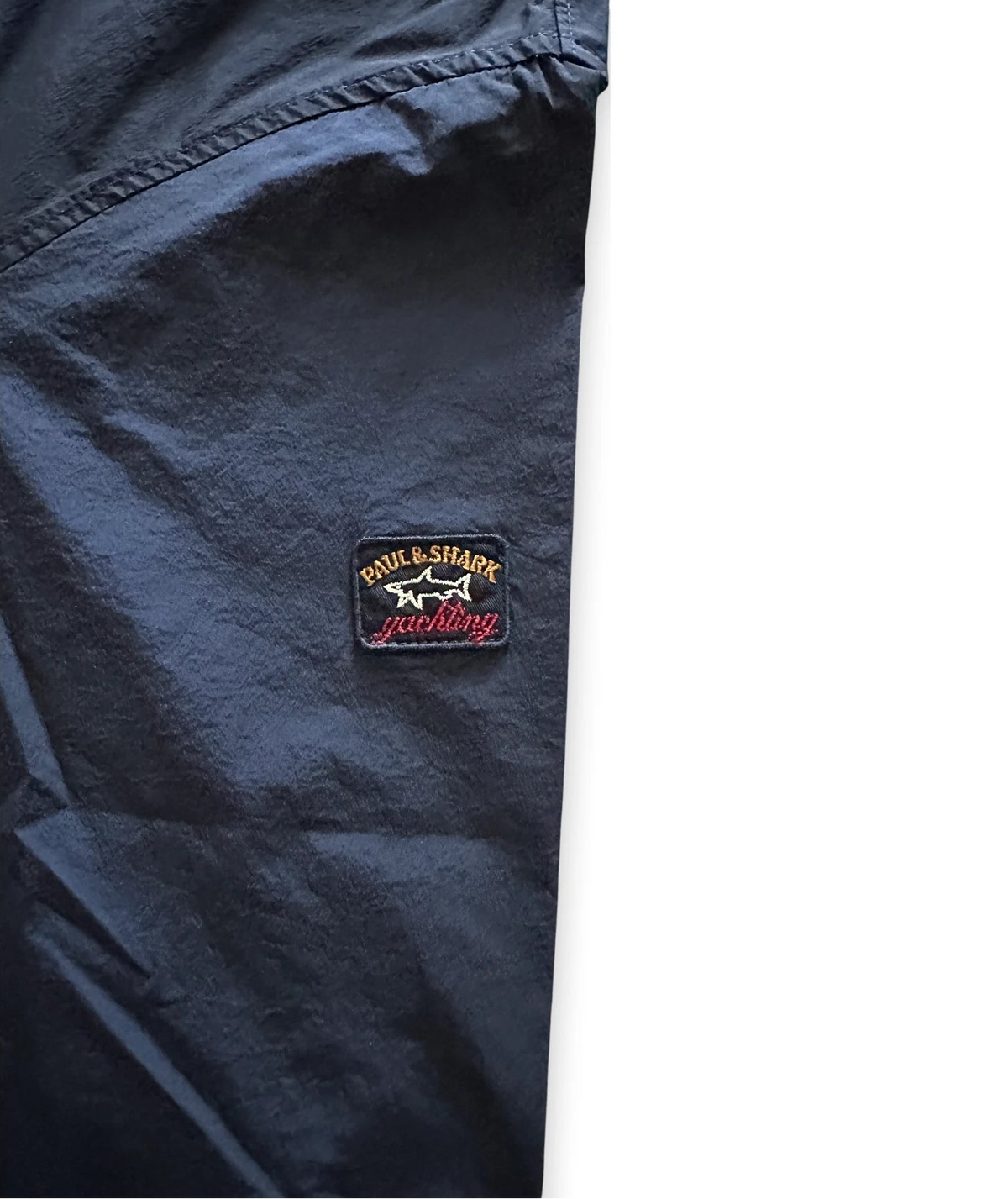 Close-up of a dark navy blue garment, likely a jacket or windbreaker, showing a small embroidered patch on the chest with the text 'Paul & Shark' and a shark logo.