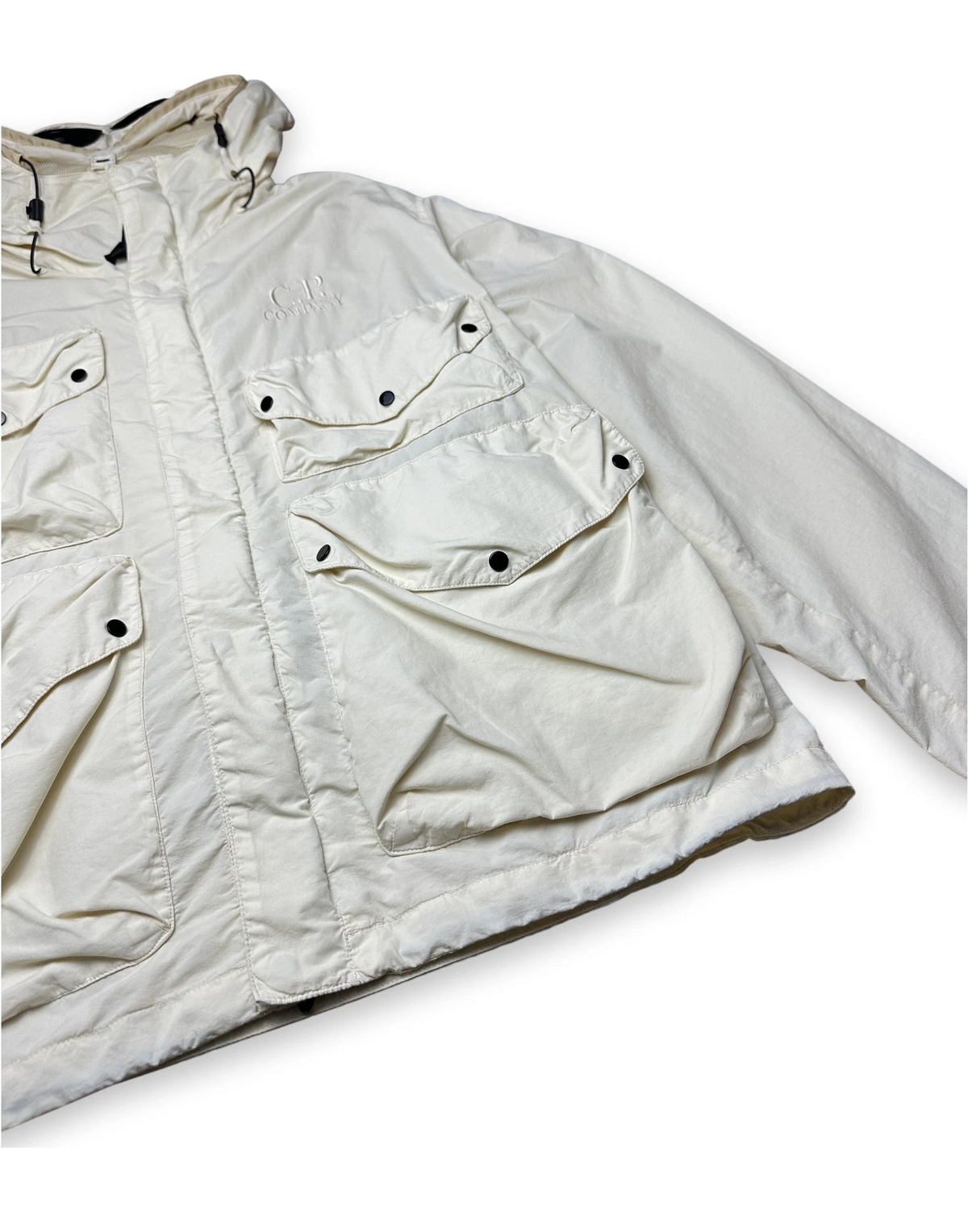 An off-white utility jacket with multiple flap pockets and snap-button details, shown on a plain white background.