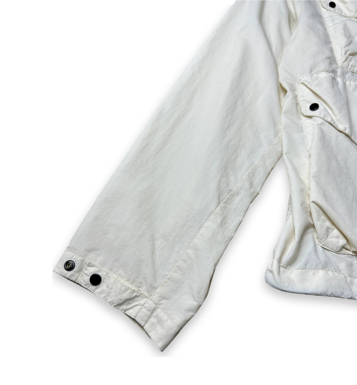 Close-up of an off-white or cream-colored jacket sleeve and side pocket with snap-button cuffs, shown on a plain white background.