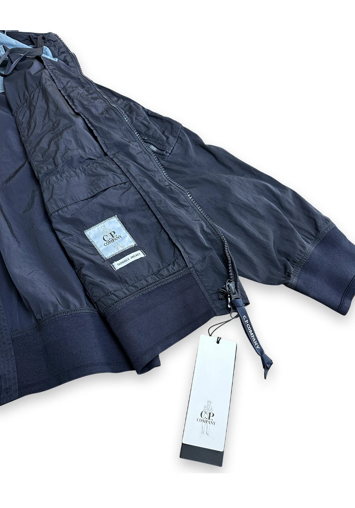 A navy blue lightweight jacket with a visible CP Company brand patch and hanging tag, photographed on a clean white background.