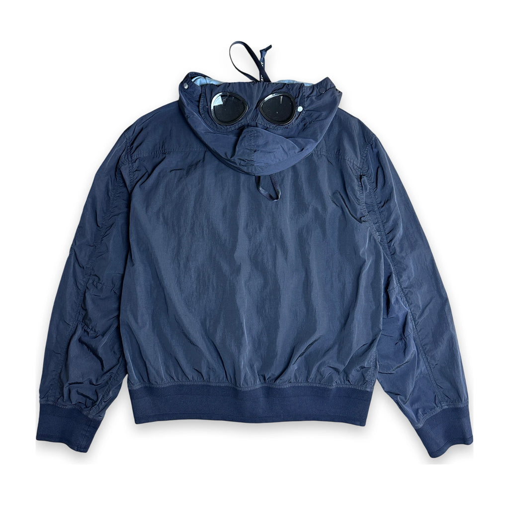 A navy blue hooded windbreaker jacket with a unique integrated hood design and sunglasses resting on the hood, displayed flat against a white background.