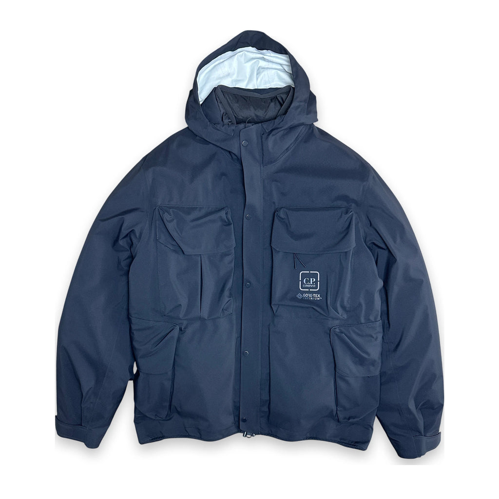 A navy blue hooded utility jacket with multiple front pockets and a small white embroidered logo patch on the left chest, displayed against a plain white background.