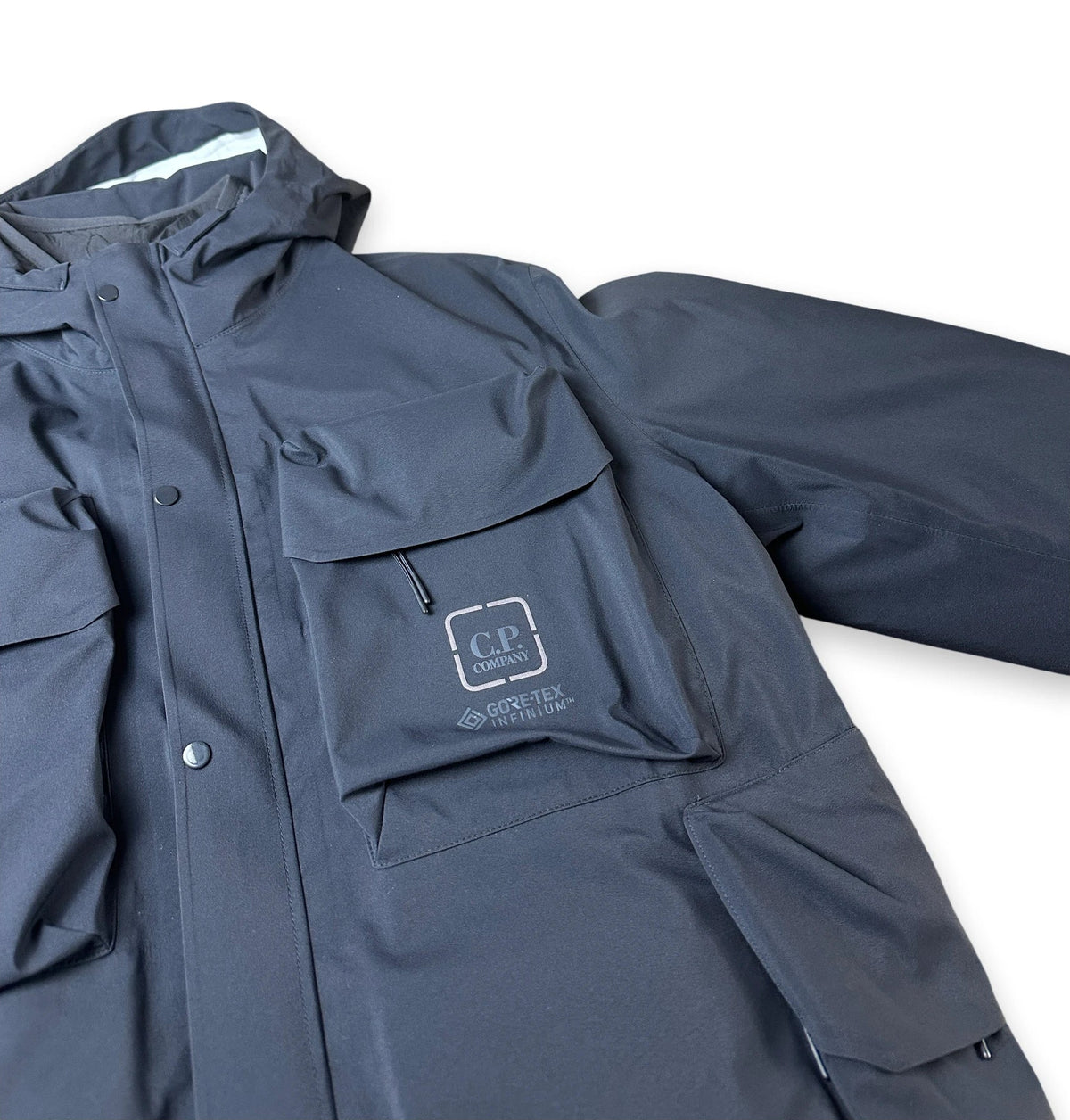 A dark slate blue waterproof jacket with multiple pockets, featuring a GORE-TEX logo patch on the chest pocket, shown against a plain white background.
