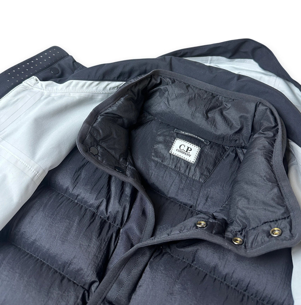 Close-up of a dark navy puffer vest with a light gray lining and a visible 'CP Company' brand label inside the collar.