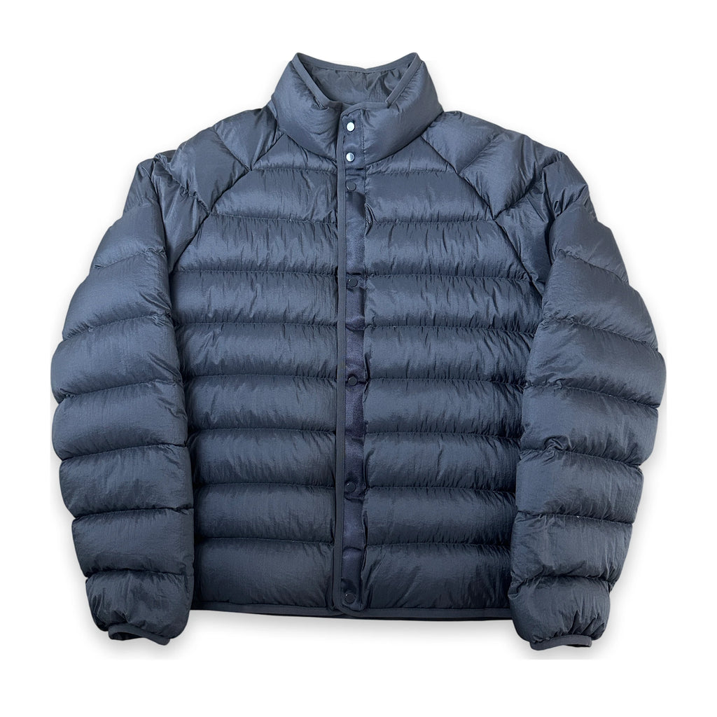 A dark slate blue puffer jacket with horizontal quilting, a stand-up collar, and a snap-button front closure, displayed against a solid white background.
