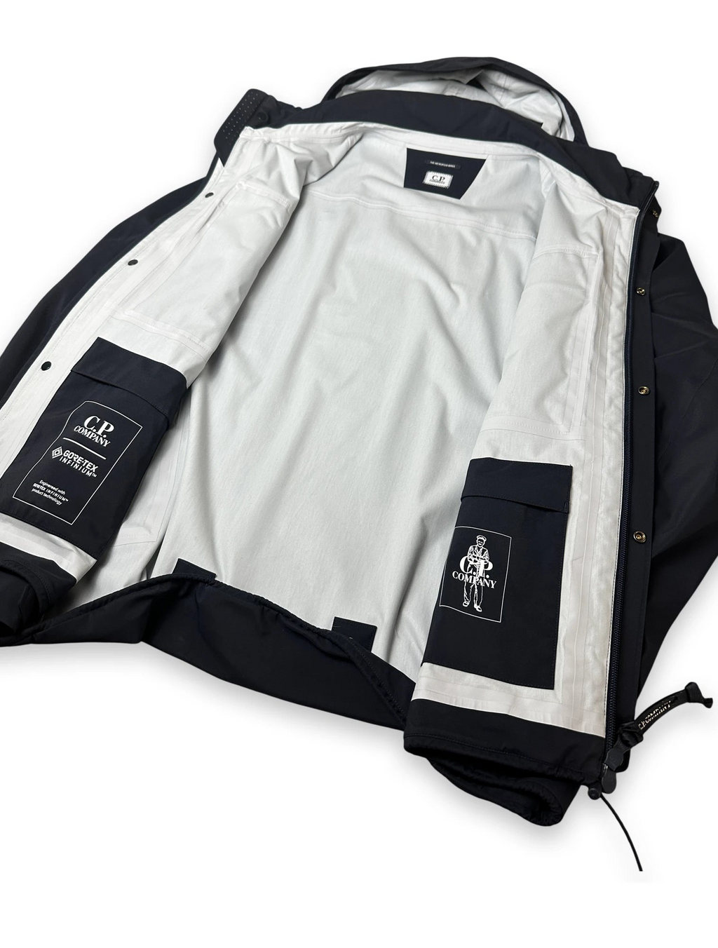 A black and white jacket shown open, with a white interior lining, black outer panels, and two visible brand patches reading G.R.