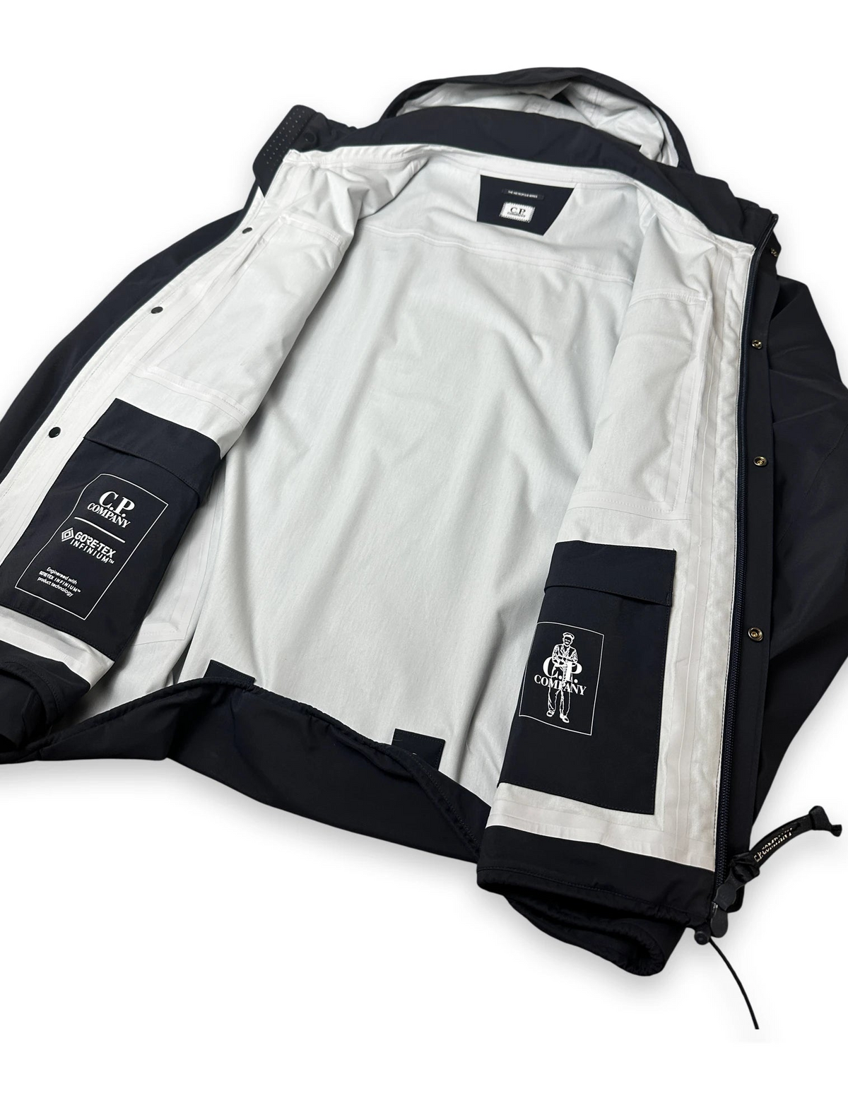 A black and white jacket shown open, with a white interior lining, black outer panels, and two visible brand patches reading G.R.