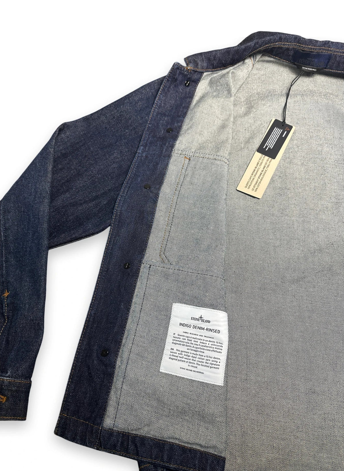 Denim jacket folded open showing its inside label of Stone Island Indigo Denim Rinse