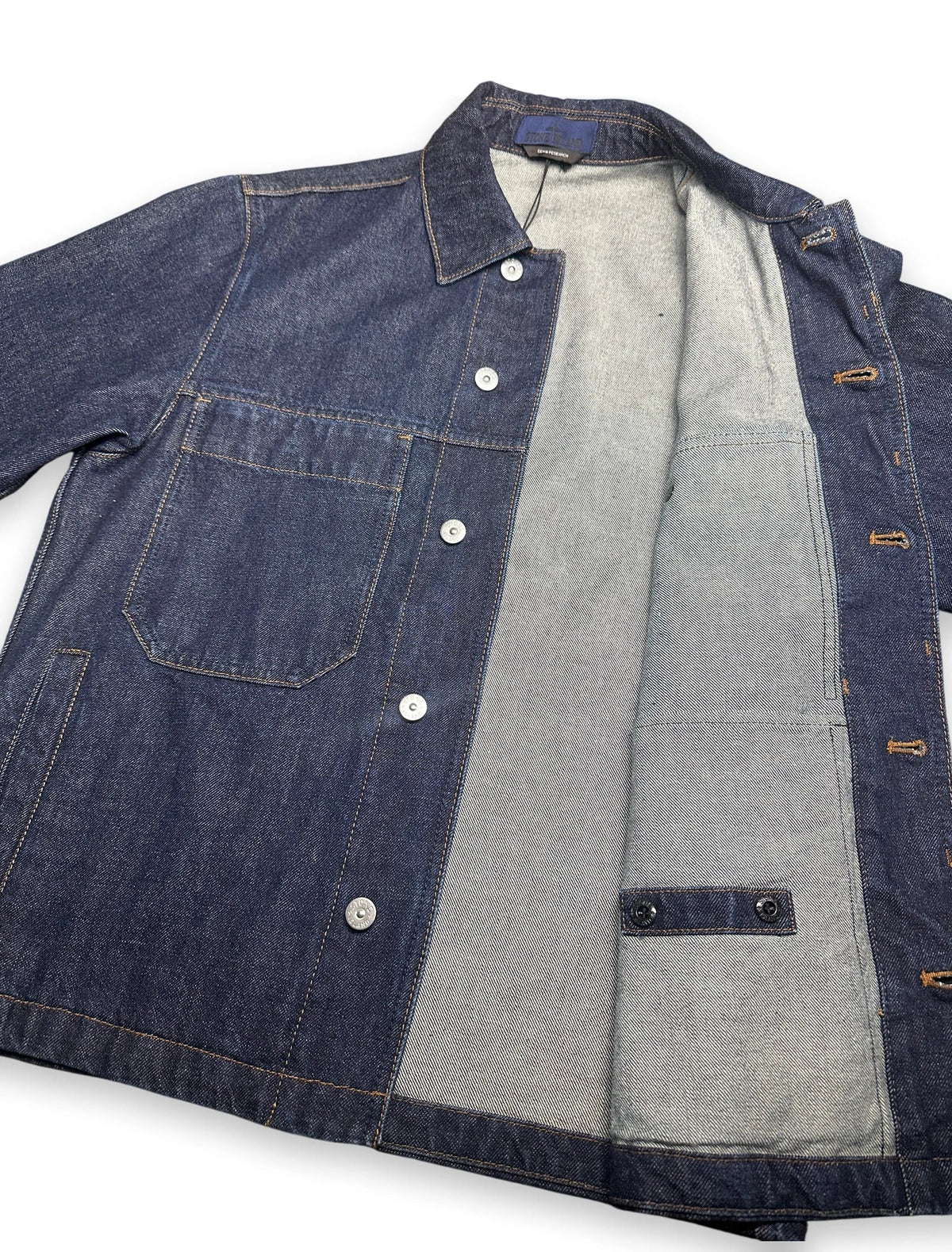 A dark indigo denim work jacket with a light gray canvas interior lining, laid flat against a white background.