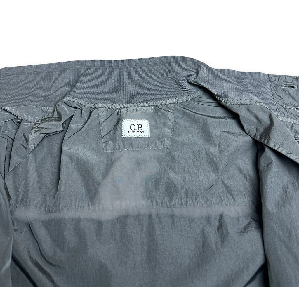 A close-up of a gray lightweight jacket or windbreaker, showing the inner collar area with a white brand label that reads 'C.P.
