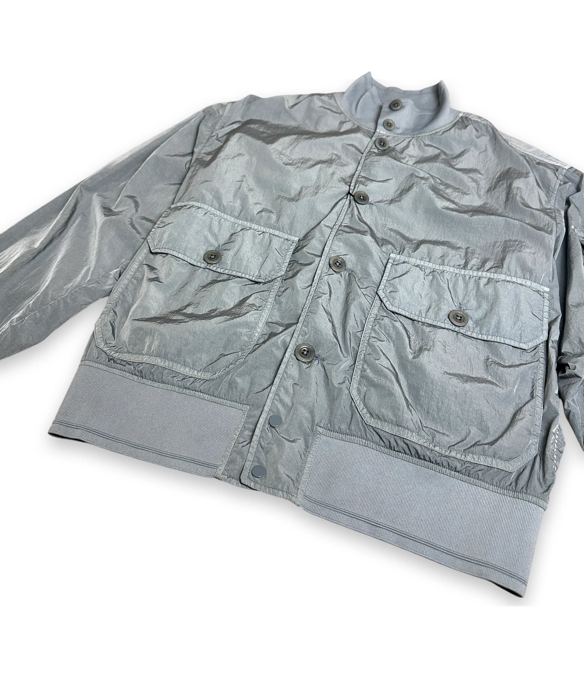 A light gray crinkled nylon utility jacket with a stand collar, button front, and two large flap chest pockets, shown on a plain white background.