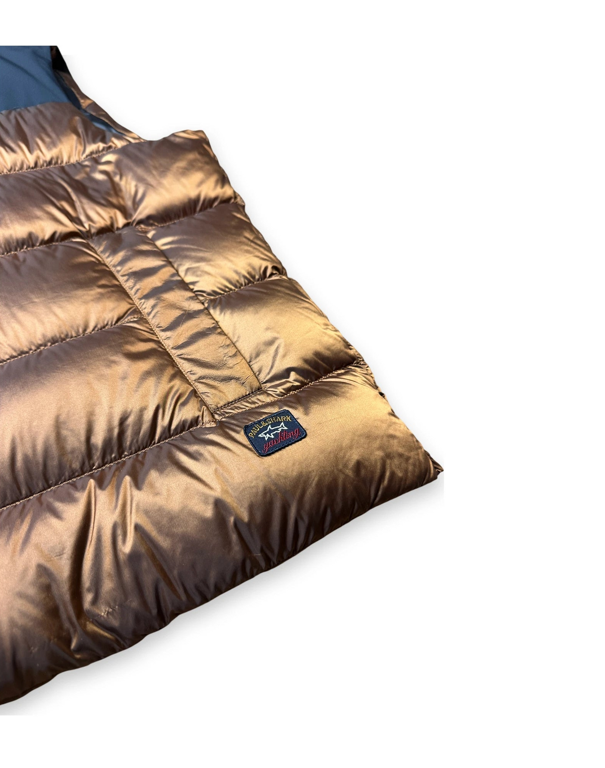 A close-up of a puffer sleeping bag showing its metallic bronze-brown shiny outer shell, quilted stitching, and a small dark brand patch on the side, set against a plain white background.