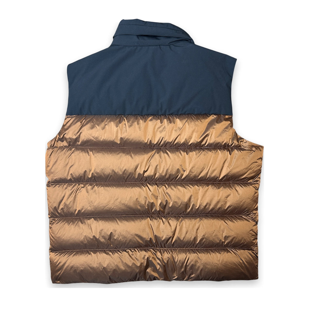 A sleeveless puffer vest shown from the back, featuring a solid navy blue upper section and a metallic bronze quilted lower section, laid flat on a white background.