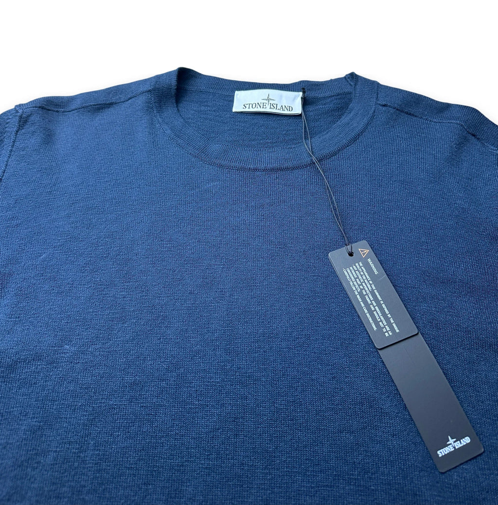 A folded dark blue knit sweater from Stone Island, featuring a black hangtag attached to the collar.