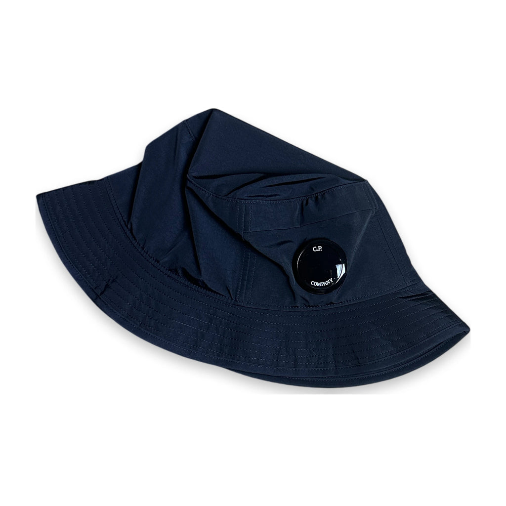 A dark navy blue sun hat with a wide brim and a small black circular logo patch on the side, displayed on a clean white background.