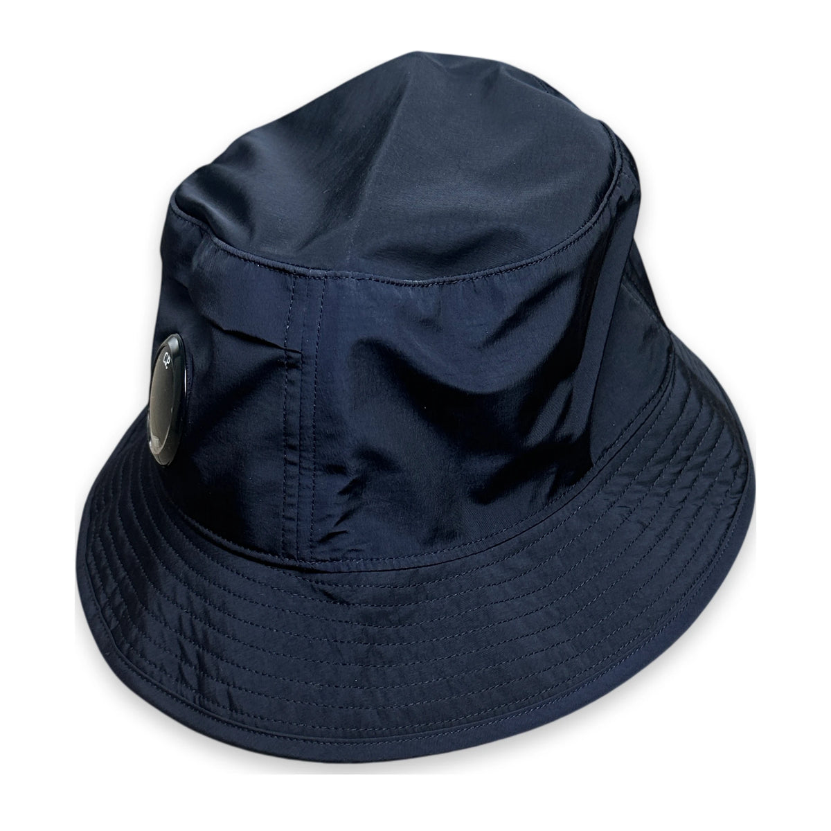 A dark navy blue bucket hat with a small circular metallic badge on the side, shown against a plain white background.