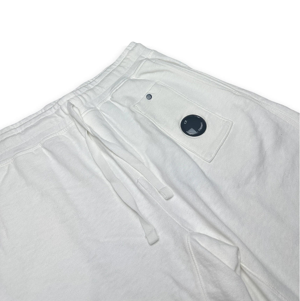 Close-up of white sweatpants showing the waistband, drawstring, and a side pocket with a black circular snap detail, photographed on a white background.