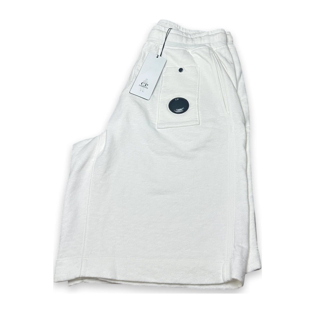Folded relaxed white shorts with a swingtag and lens of C.P. Company on a white background