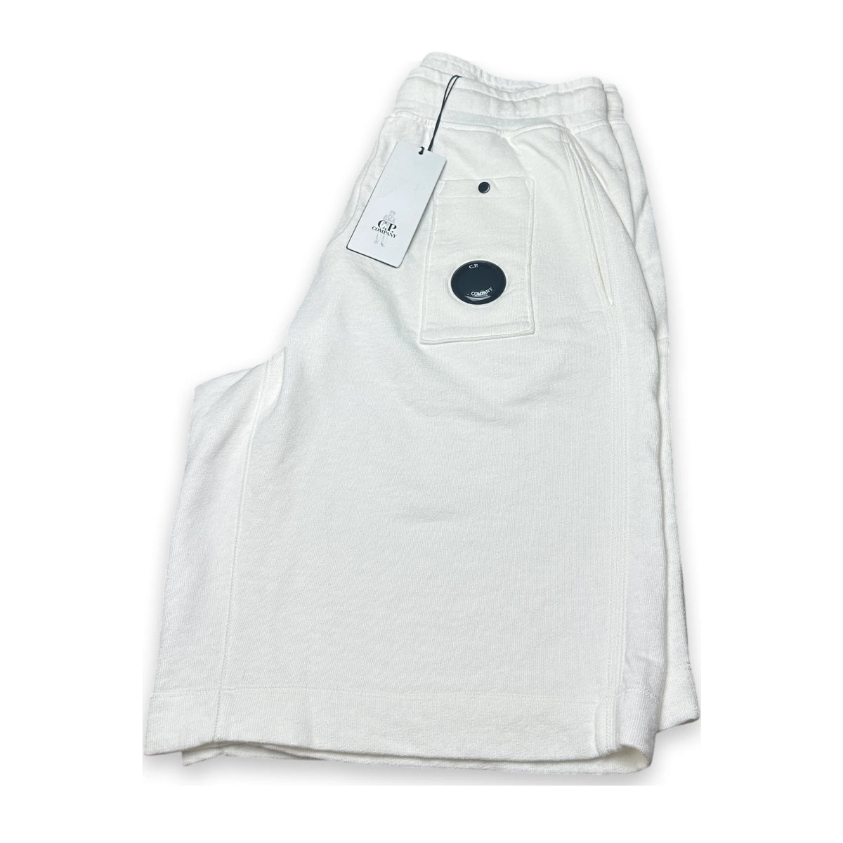 Folded relaxed white shorts with a swingtag and lens of C.P. Company on a white background