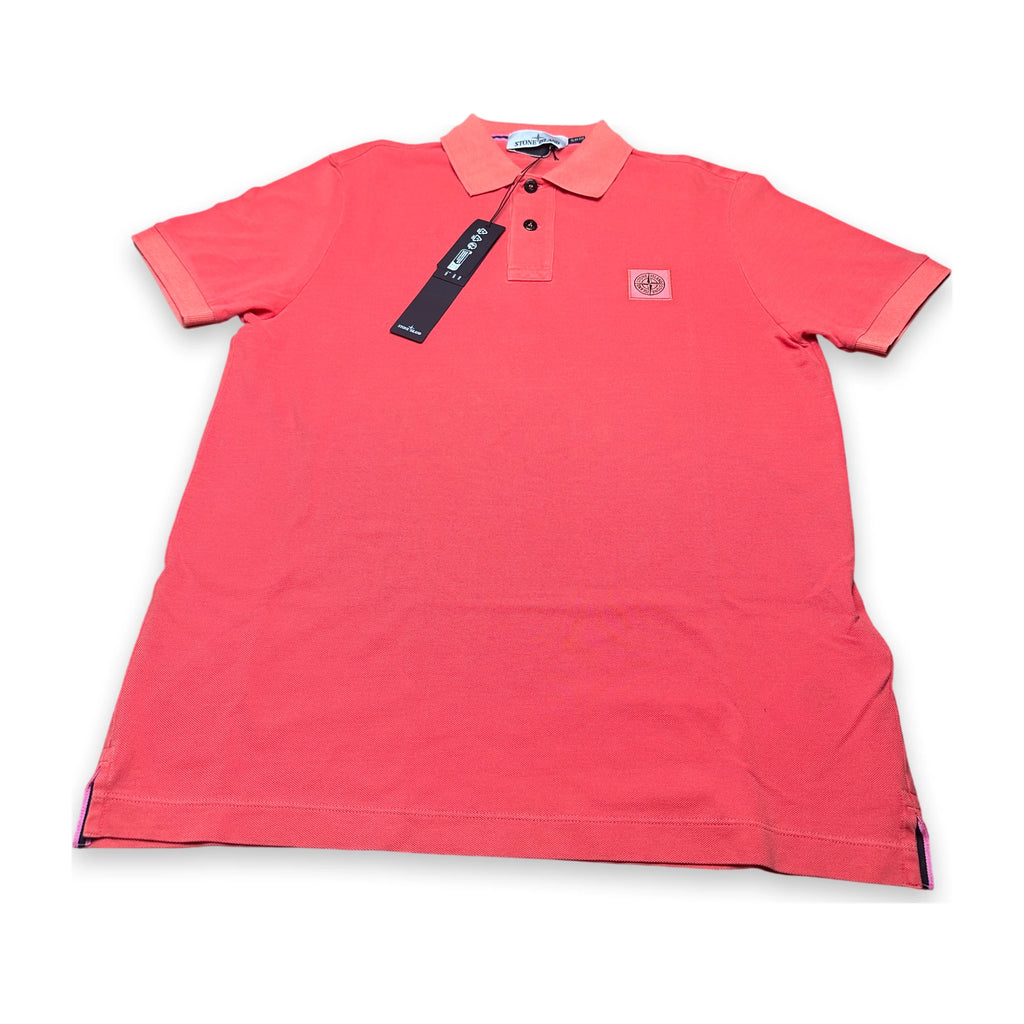 A coral pink short-sleeve polo shirt with a collar and three-button placket, featuring a small circular chest logo and a black hangtag, laid flat on a white background.