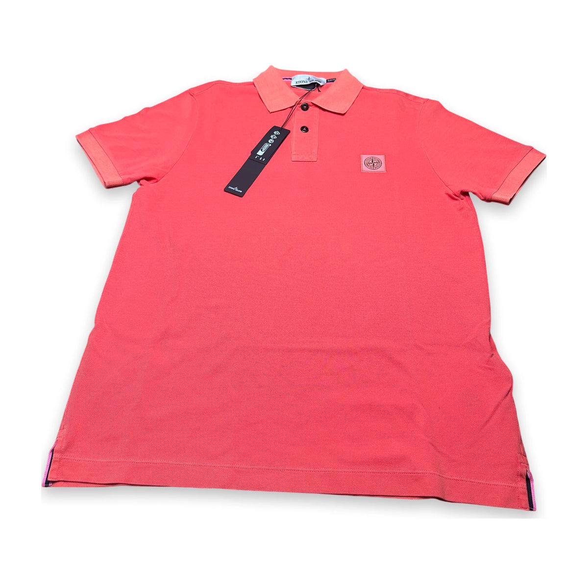 A coral pink short-sleeve polo shirt with a collar and three-button placket, featuring a small circular chest logo and a black hangtag, laid flat on a white background.
