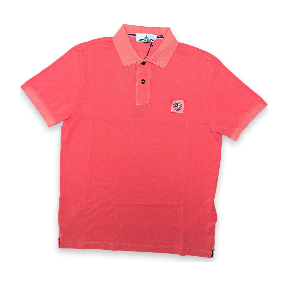 A coral pink short-sleeve polo shirt with a three-button placket and a small circular compass logo patch on the left chest, displayed flat against a white background.