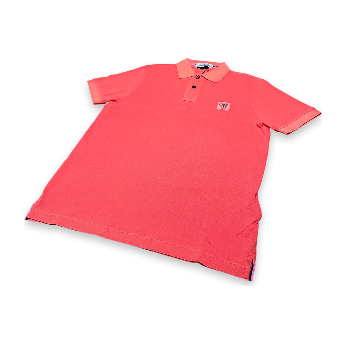 A coral pink short-sleeve polo shirt with a two-button placket and a small square logo patch on the left chest, displayed flat against a white background.